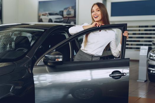 Beautiful young woman touching her new car with pleasure and joy