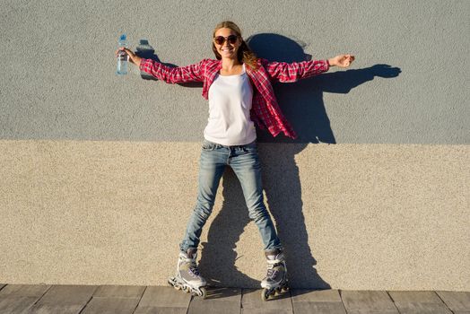 A beauty teen model girl, shod in rollerblades holding a water bottle. Sports, health and active leisure.