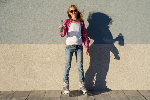 A beauty teen model girl, shod in rollerblades holding a water bottle. Sports, health and active leisure.