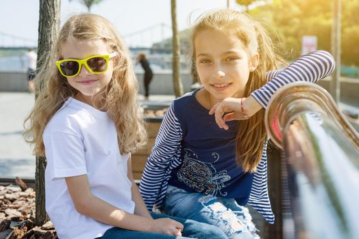Two pretty little girls are looking at the camera and smiling. Background urban, summer, embankment of the river