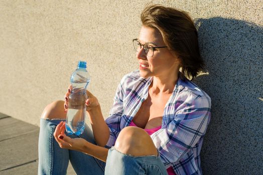 Adult healthy woman drinks water from bottle. Outdoor