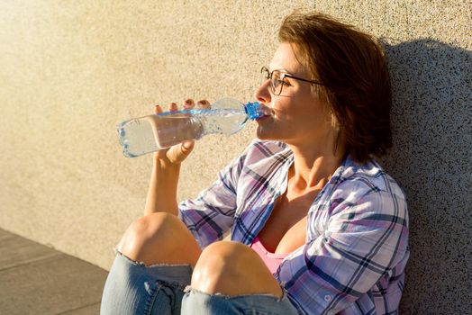 Adult healthy woman drinks water from bottle. Outdoor portrait.