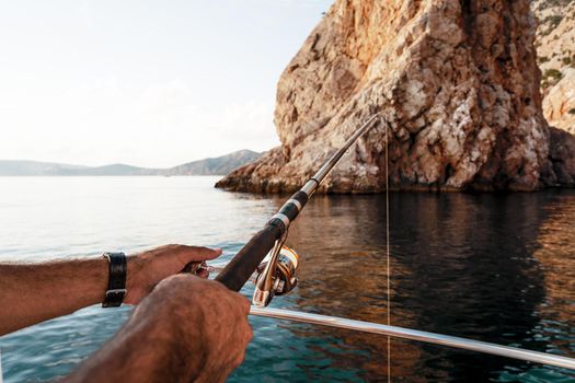 Close up photo of male hands holding fishing rod while fishing on sailboat in open sea