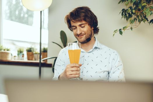 Bearded man using his laptop while drinking glass of beer sitting at his table