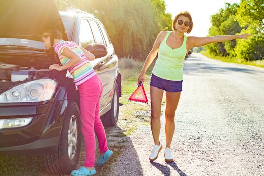 Woman driver with her teenage daughter on country road, near broken car.