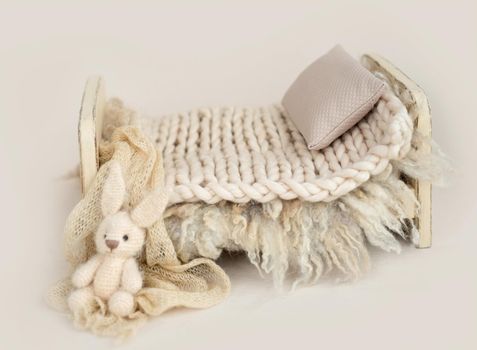 Wooden stylized small furniture bed with pillow and knitted blanket for newborn photoshoot in beige colors. Designed decoration object for infant studio photo