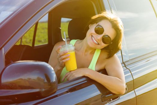 Happy female driver smiling to you. Stop to relax, enjoy the journey, drink orange juice.