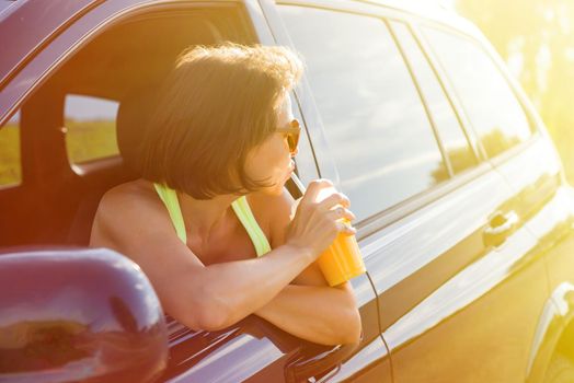 A happy woman driver stops to relax, enjoy the journey, drink orange juice. Do not look at the camera