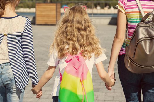 Rear view of three girls' children. They hold hands, walk in the city. Background of an urban summer