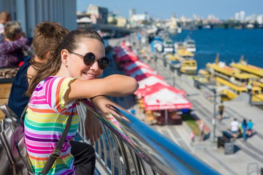 Smiling teenage student girl standing on the embankment near the river.