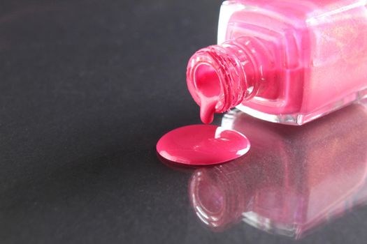 Pink nail polish is poured out of the bottle bottle on a black background with a copyspace place for text.