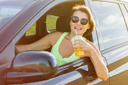 Happy female driver smiling to you. Stop to relax, enjoy the journey, drink orange juice.
