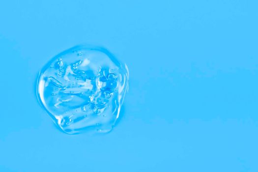 Clear transparent liquid gel drop or smear isolated on blue background. Top view. Virus protection or cosmetics concept. Serum texture. Banner with copy space.