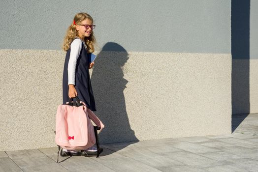 A schoolgirl of elementary school with notebooks in his hand. A girl with a backpack goes to school. Back to school