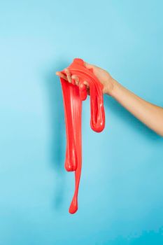 Close up on shiny Red or coral slime in the hand isolated on blue background. Fun and stress relief concept. Vertical banner.
