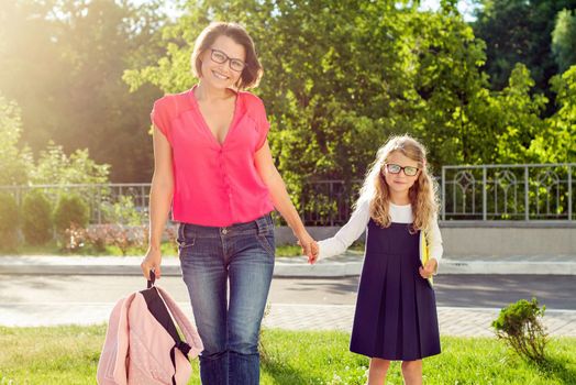 Mom and pupil of elementary school holding hands. The parent takes the child to school. Outdoors, return to the concept of the school.