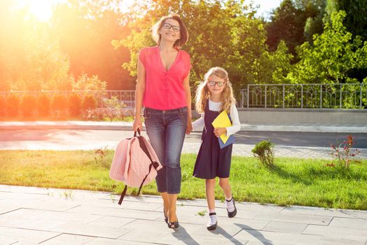 Mom and schoolgirl of primary school holding hands. The parent takes the child to school. Outdoors, return to the concept of the school