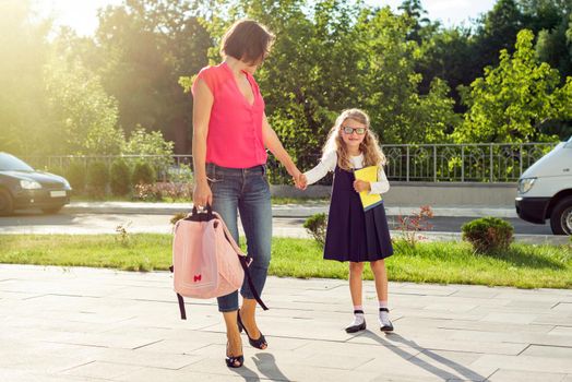 Mom and pupil of elementary school holding hands. The parent takes the child to school. Outdoors, return to the concept of the school.