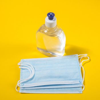 Alcohol gel hand sanitizer and disposable hygienic mask on yellow background