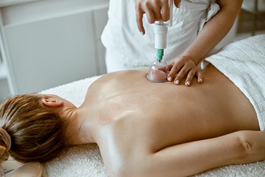 professional female specialist is doing cupping therapy on the back of beautiful caucasian lady