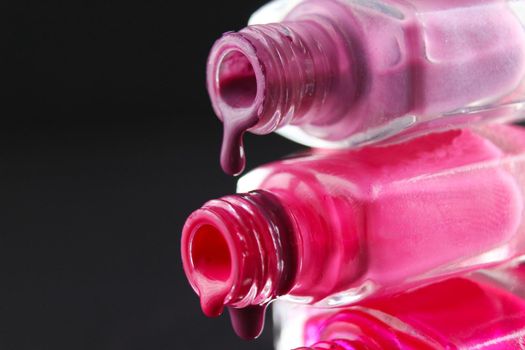 drops of red bearded pink nail polish flow from the bottle of the bottle on a black dark background with a copyspace.