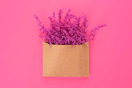 Bright purple or violet lavender flowers in craft brown envelope with copy space isolated on pink background. Trendy monochrome banner for Valentines Day or International Womens Day .