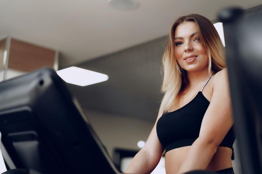 Fit curvy young blonde woman training in a cardio zone in a gym close up