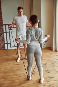 Sporty man and woman are doing training with resistance bands in living room during quarantine