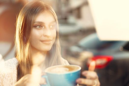 Portrait of a young woman having a cup of coffee and looking through the window. Close up.