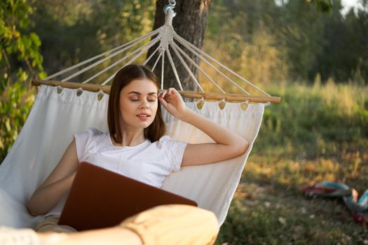 cheerful woman lies in a hammock with a laptop vacation internet travel. High quality photo