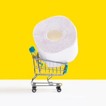 Toy shopping cart or trolley with large roll of toilet paper isolated on yellow background. Sale concept