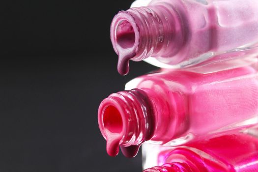 drops of red bearded pink nail polish flow from the bottle of the bottle on a black dark background with a copyspace.