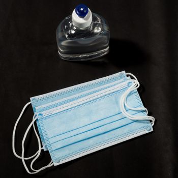 Alcohol gel hand sanitizer and disposable hygienic mask on black background