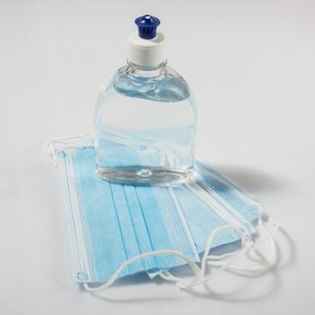 Alcohol gel hand sanitizer and disposable hygienic mask on gray background