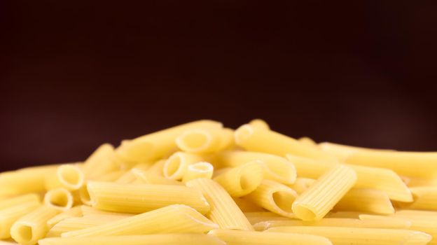 Penne Rigate Raw Pasta is a short pasta with oblique cuts and a ribbed surface. Traditional Italian pasta. Pasta background. Italian food ingredient side view