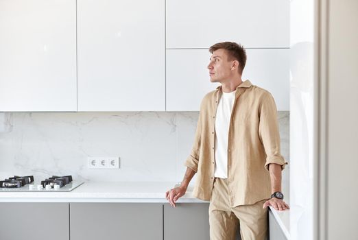 Happy handsome man is standing on minimalistic kitchen and smiling