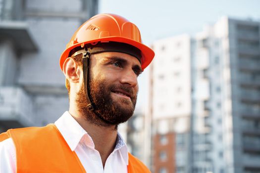 Builder wearing hardhat and safety vest standing on a commercial construction site, close up portrait