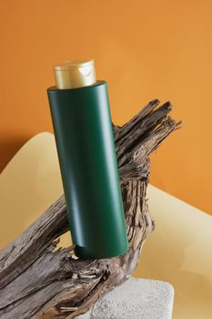 green bottle for shampoo or hair balm on a concrete podium on a wooden driftwood background, brown background, mock up cosmetic