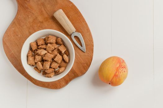 brakefast with chocolate pillows and peach with knife. Crispy cereal and chocolate pillows with milk. Flat lay. wooden table and white background.