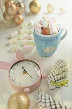 cute cup adorned with pink marshmallow and pink clock, christmas decorations. time before party. tasty sweeties and mug with cinnamon and candies.