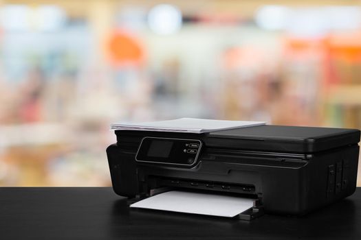 Compact laser printer on black desk against blurred background, close up