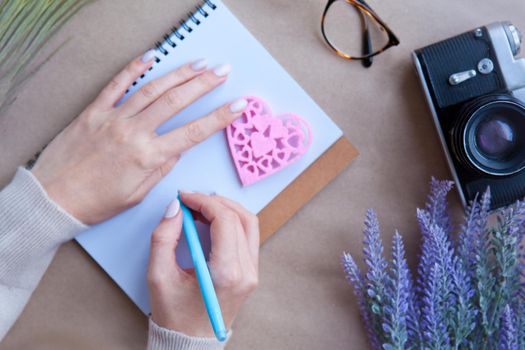 Wooden heart LOVE and woman hands behind notebook on the table and retro camera. Letter writting concept. Heart shape symbol. Valentines - romantic greeting and letters lifestyle feelings concept