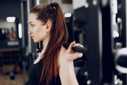 Young woman doing squats with barbell in a gym apparatus close up