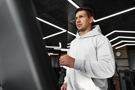 Portrait of a young man in orange windbreaker workout on a fitness machine at a gym.