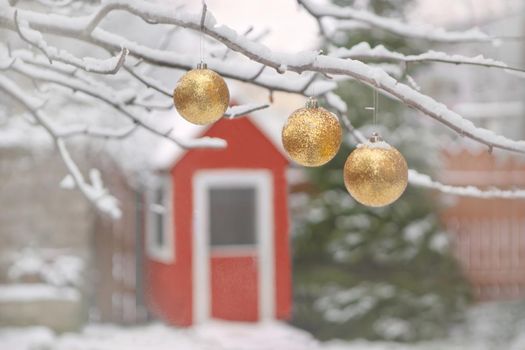 golden christmas tree balls on tree branches and winter snow. Christmas balls near fur-trees covered with a snow and small red wooden house.