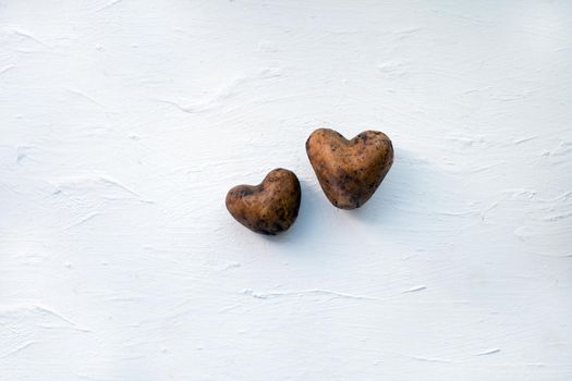 Two raw potatoes on the white wooden background. Potatoes like a heart. Ecology love concept. Fresh food products.