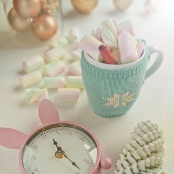 cute cup adorned with pink marshmallow and pink clock, christmas decorations. time before party. tasty sweeties and mug with cinnamon and candies.
