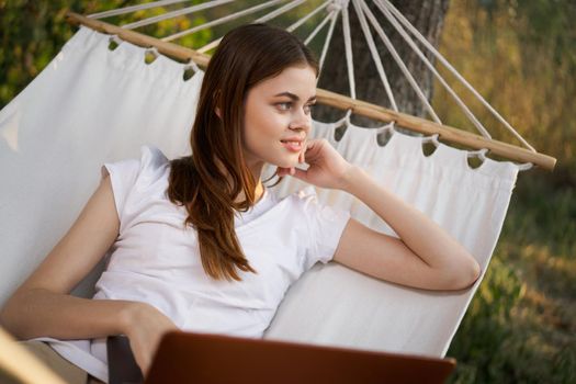cheerful woman lies in a hammock with a laptop freelance nature. High quality photo