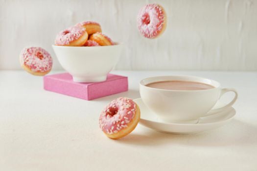 Flying pink donuts with a cup of cacao on a white background. selective focus on sweet pink flying donuts, Tasty Junk food concept