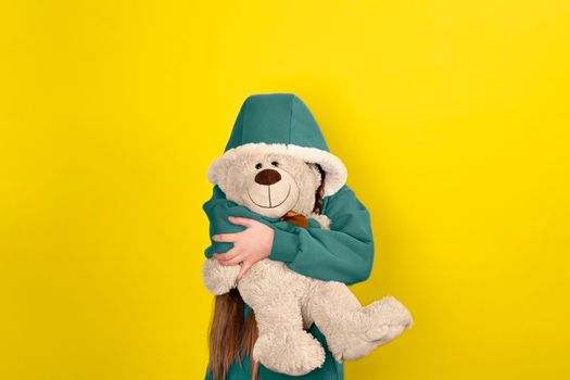 Teen beautiful girl hugs and hide behind big teddy bear. Banner with copy space. Child girl in modern clothes